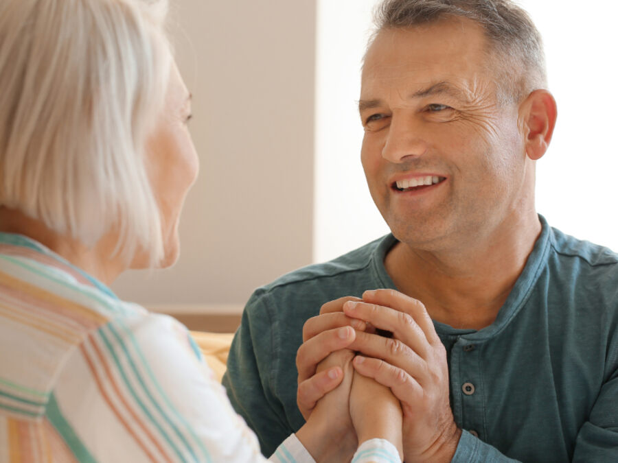 Senhora idosa de mãos dadas com o marido, a conversar em casa